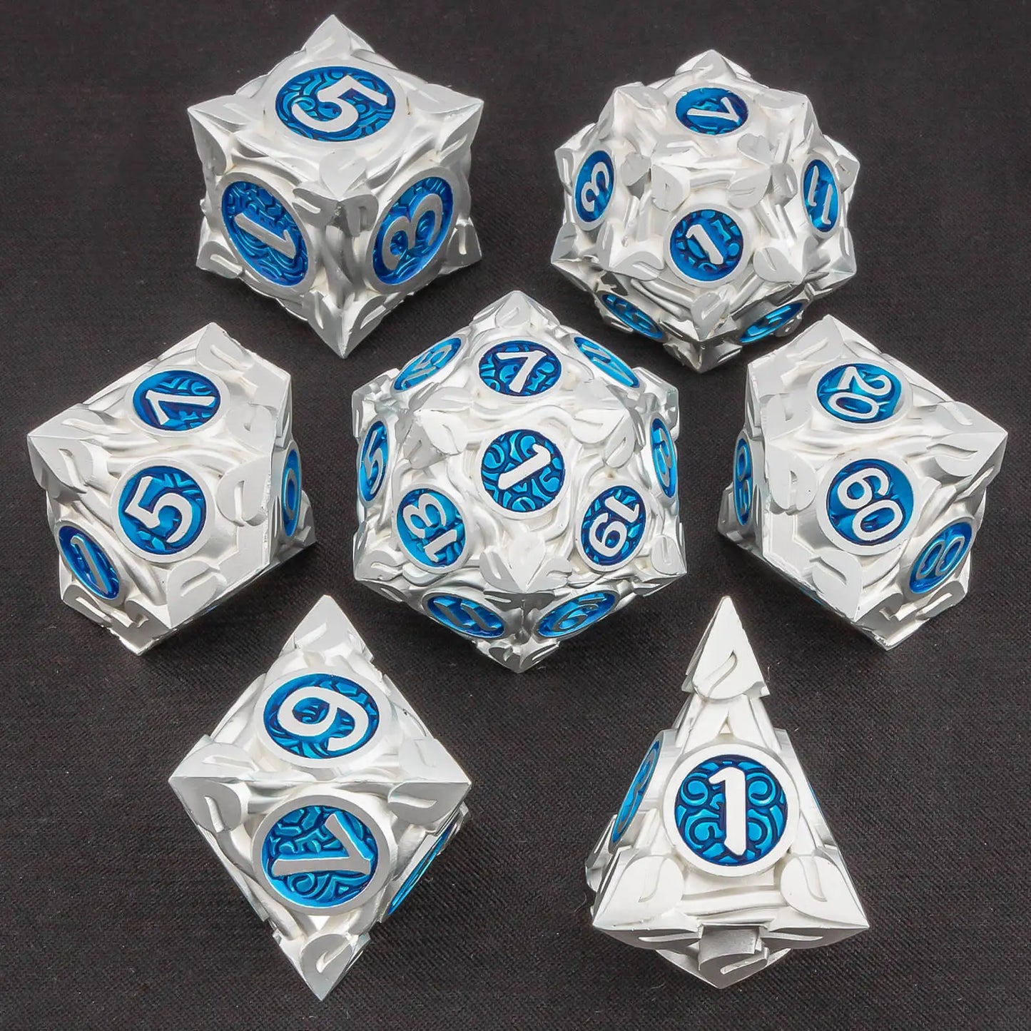 A set of metallic silver polyhedral gaming dice with blue circular faces displaying white numbers, arranged on a dark textured background.