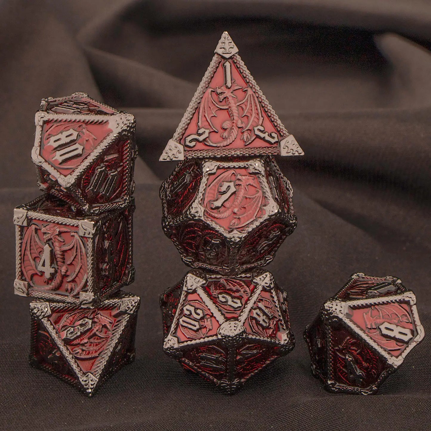 A set of metal red and dark silver fantasy-themed polyhedral dice with ornate dragon illustrations, arranged on a dark draped fabric background.