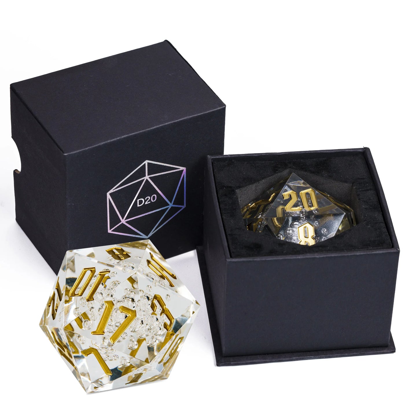 A clear acrylic d20 polyhedral die with gold numbering, shown alongside its open black presentation box and a closed black box with a D20 icon.