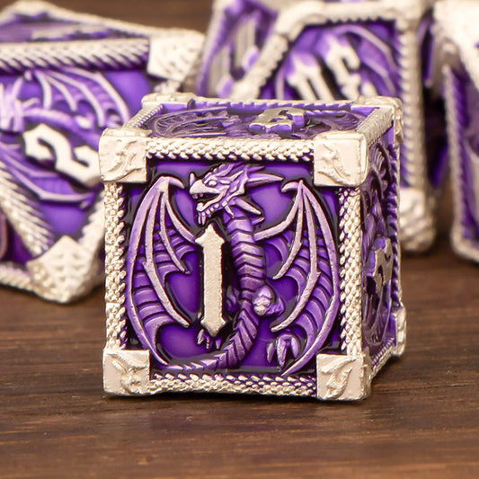 A purple and silver fantasy dice box featuring an embossed dragon design on the front, displayed on a wooden surface with other matching dice blurred in the background.