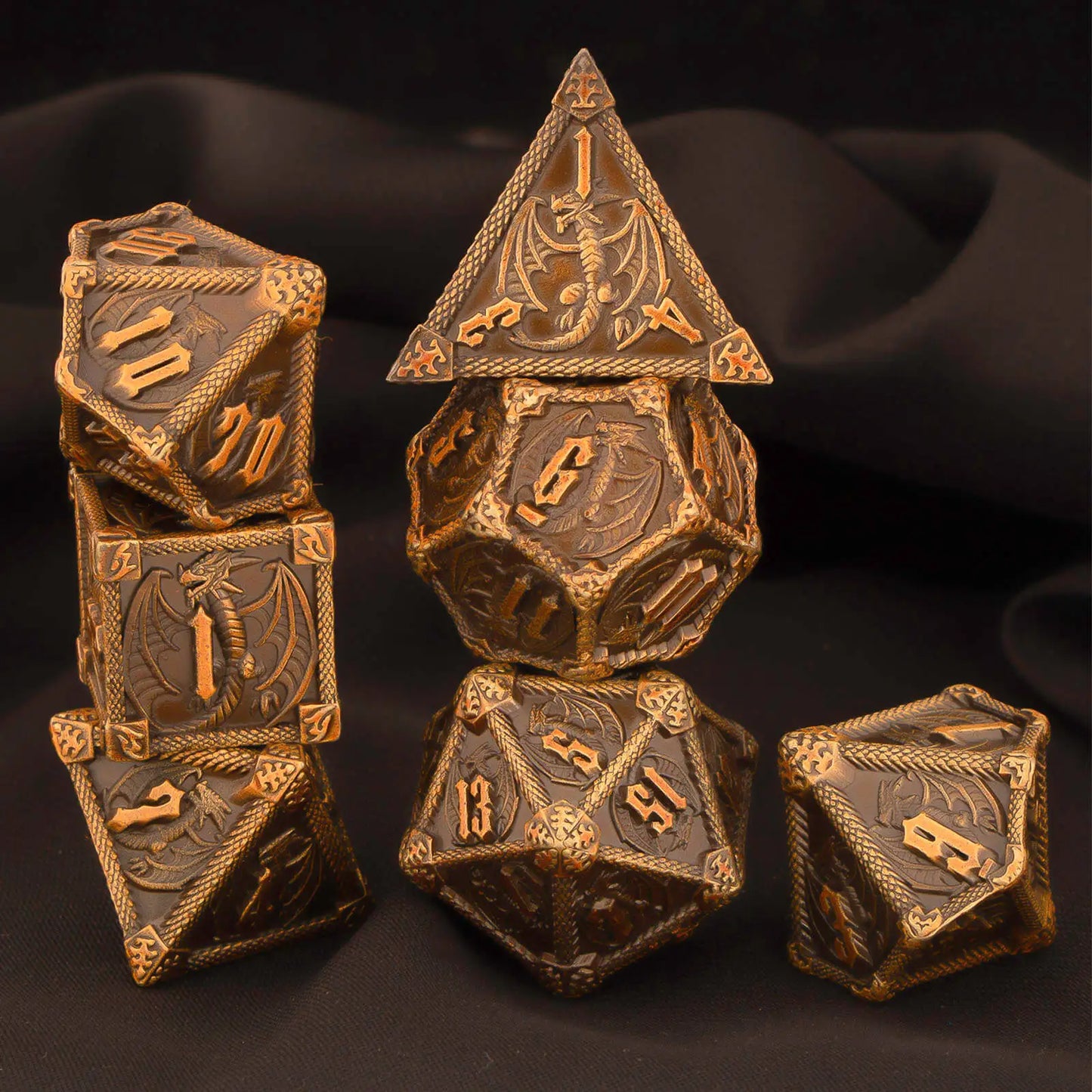 A set of metal dragon-themed polyhedral gaming dice with a dark bronze and gold finish, arranged on a black fabric background.