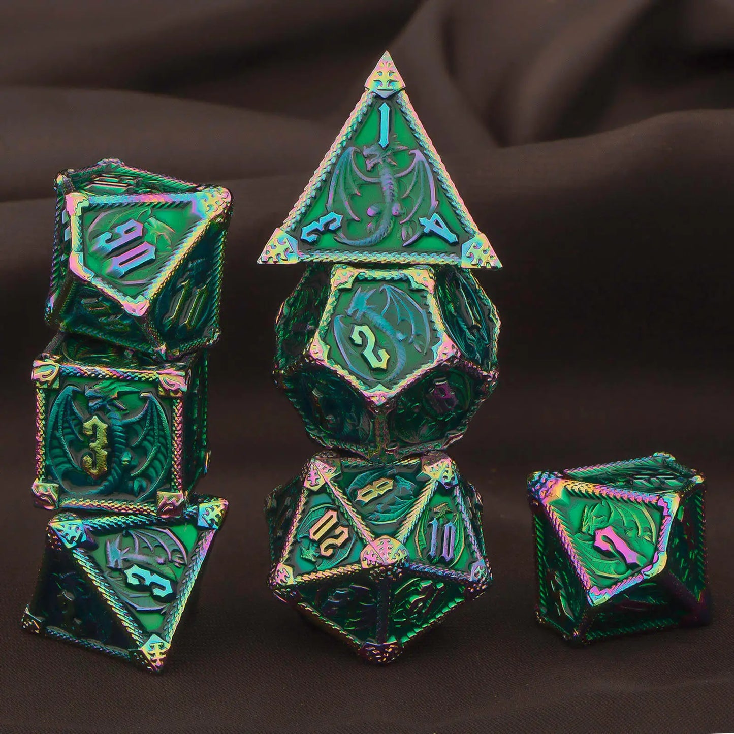 A set of metal polyhedral gaming dice with an iridescent green and rainbow finish, arranged on a dark brown draped fabric background. Includes a d4, d6, d8, d10, d%, d12, and d20.