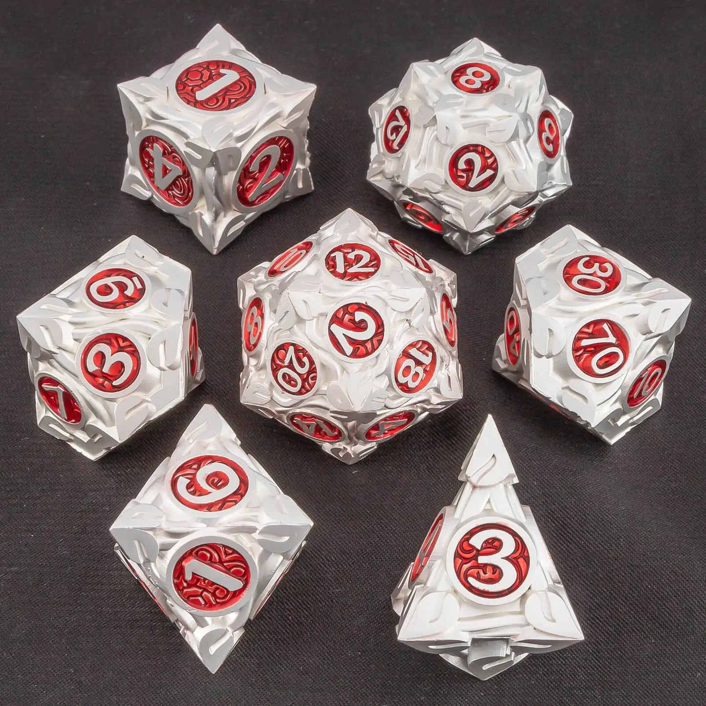 A set of metallic silver polyhedral gaming dice with red circular faces displaying white numbers, arranged on a dark textured background.