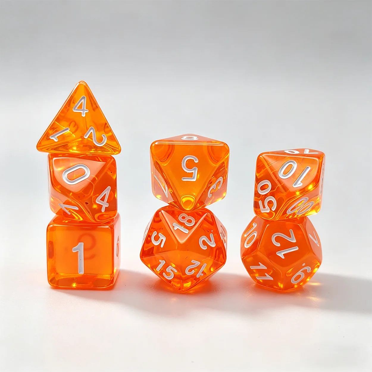 A set of translucent orange polyhedral dice with white printed numbers, arranged on a light gray studio background.