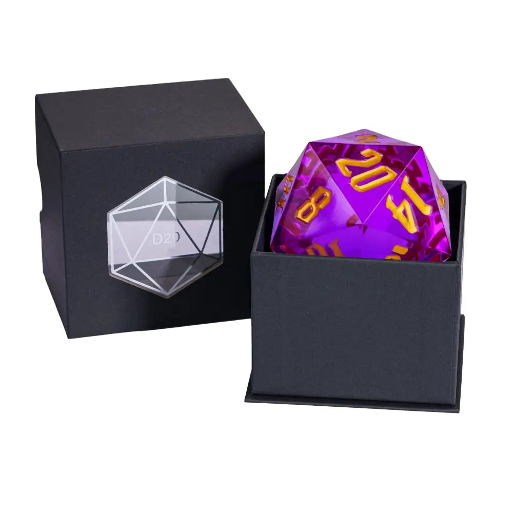 A translucent purple 20-sided die with gold numbering displayed in an open black presentation box, alongside a closed black box with a clear engraved 20-sided die icon on the front.