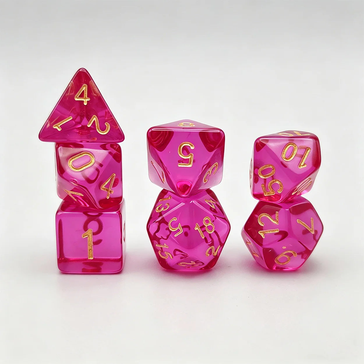 A set of translucent pink polyhedral gaming dice with shiny gold numbers, arranged on a clean white background.