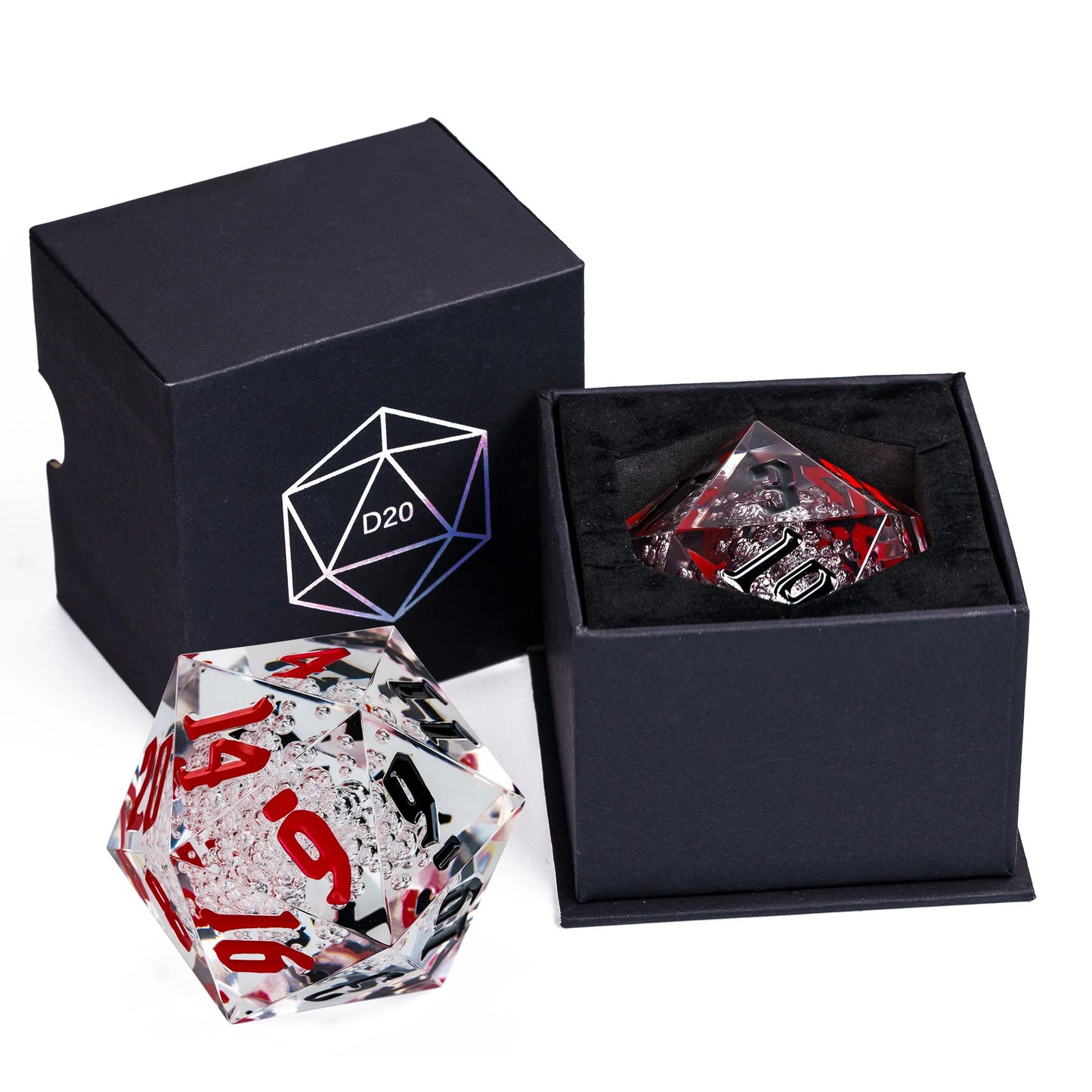 A clear acrylic D20 polyhedral die with red and black printed numbering, shown alongside its black presentation box and an open box containing a matching die.