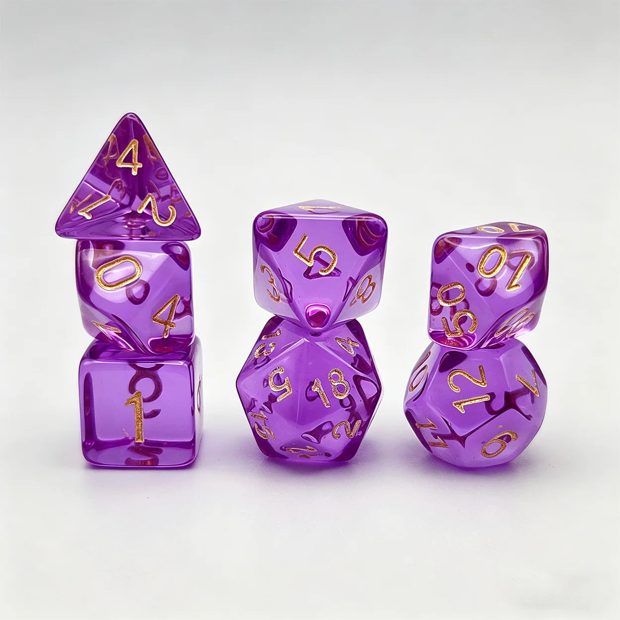 A set of translucent purple polyhedral gaming dice with shiny gold numbers, arranged on a clean white background.