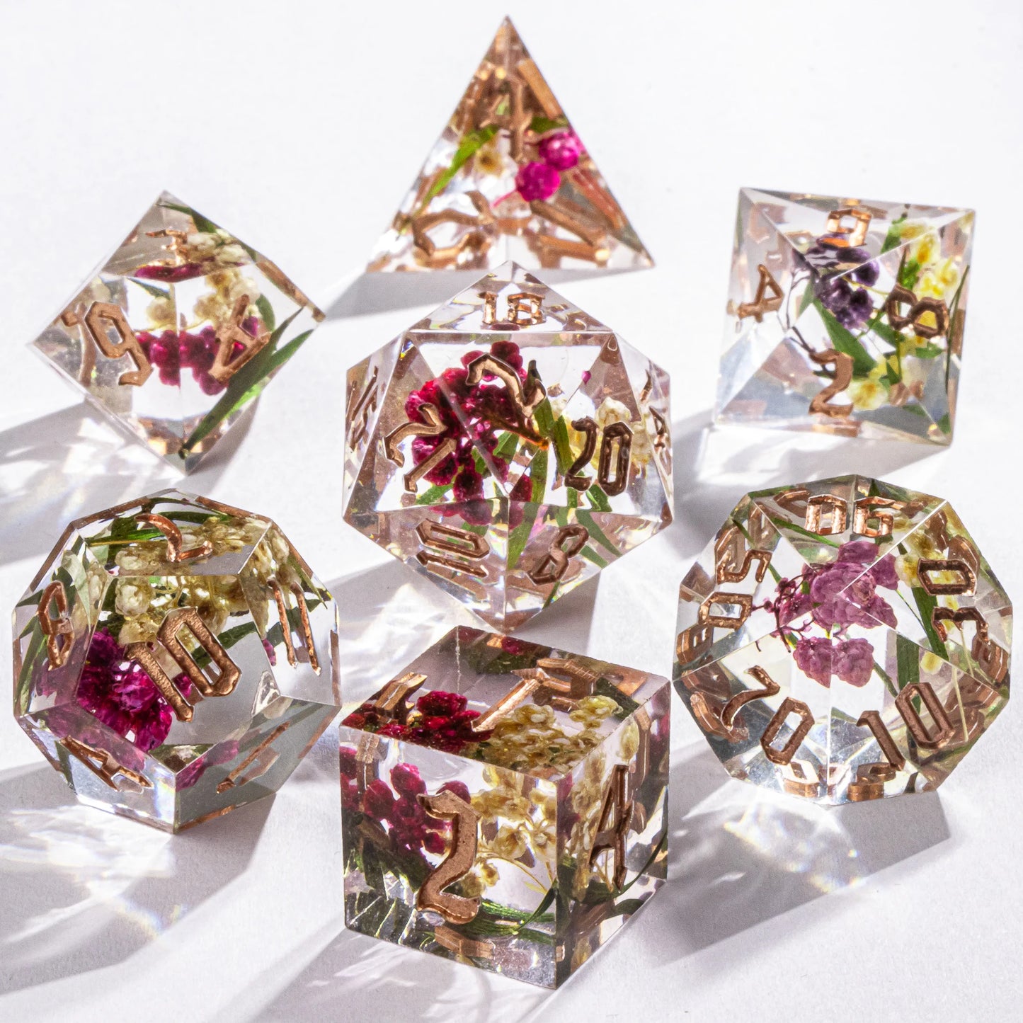 Set of clear polyhedral dice with floral and gold accents on a white background