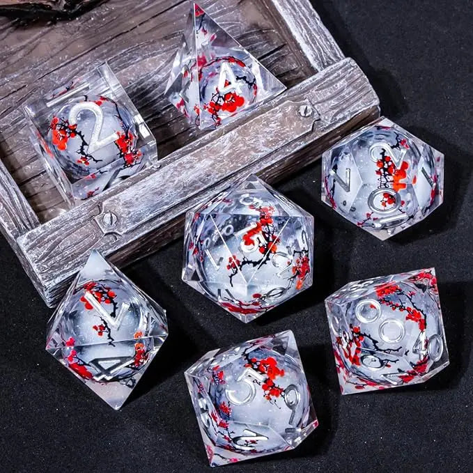 A set of transparent acrylic polyhedral gaming dice a liquid clore, containing white glitter, with red and black floral inlay, silver numbering, displayed on a rustic wooden tray and dark surface.