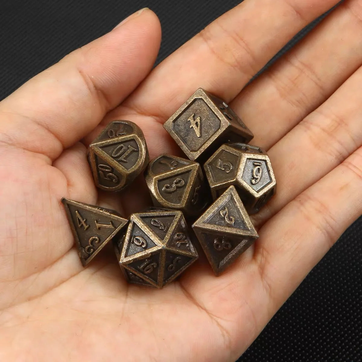 Hand holding bronze polyhedral dice with numbers on a black background