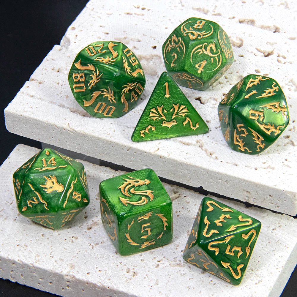 A set of green polyhedral gaming dice with gold dragon illustrations, arranged on a white textured stone slab against a black background.