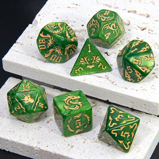 A set of green polyhedral gaming dice with gold dragon illustrations, arranged on a white textured stone slab against a black background.