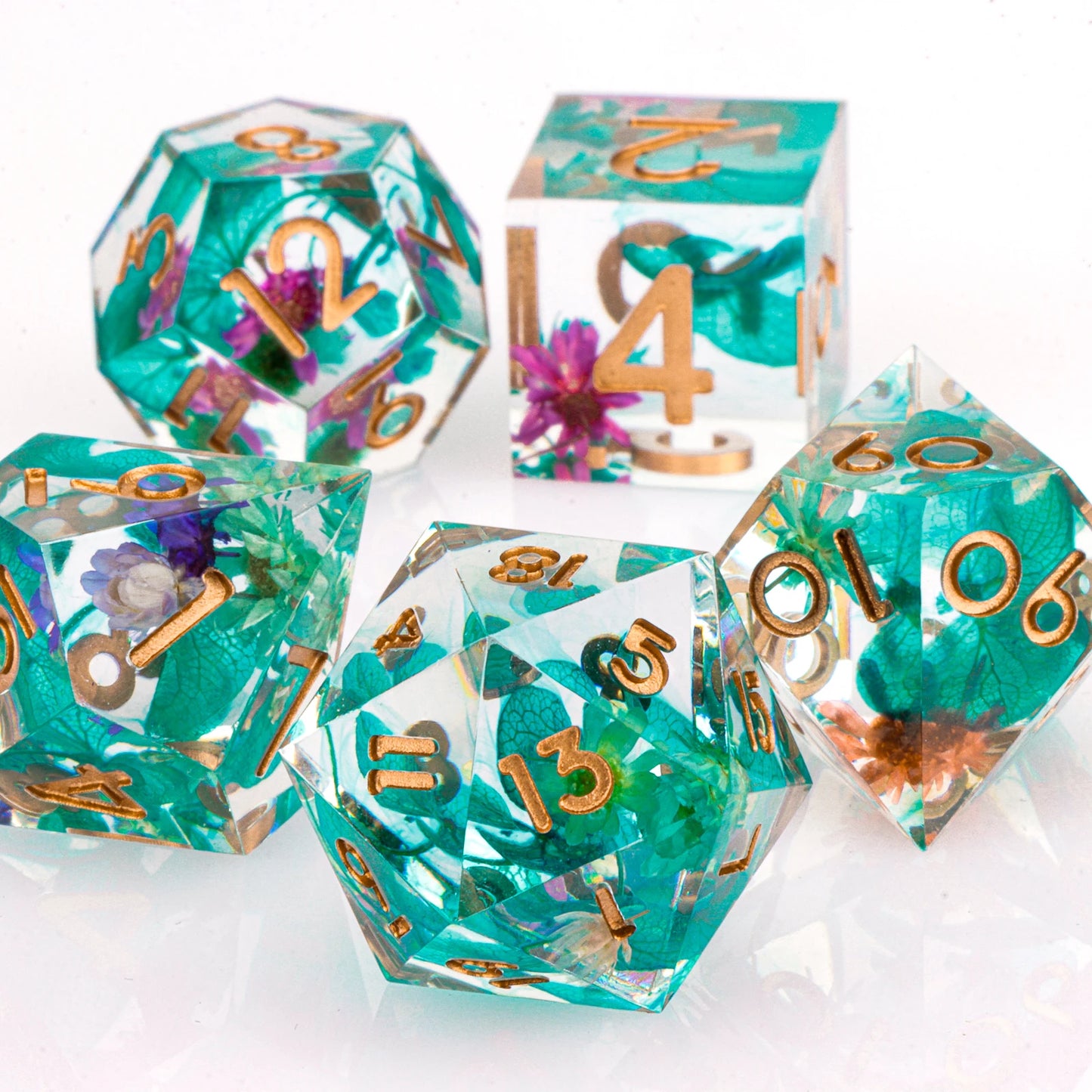 Set of teal and gold polyhedral dice with floral elements on a white background