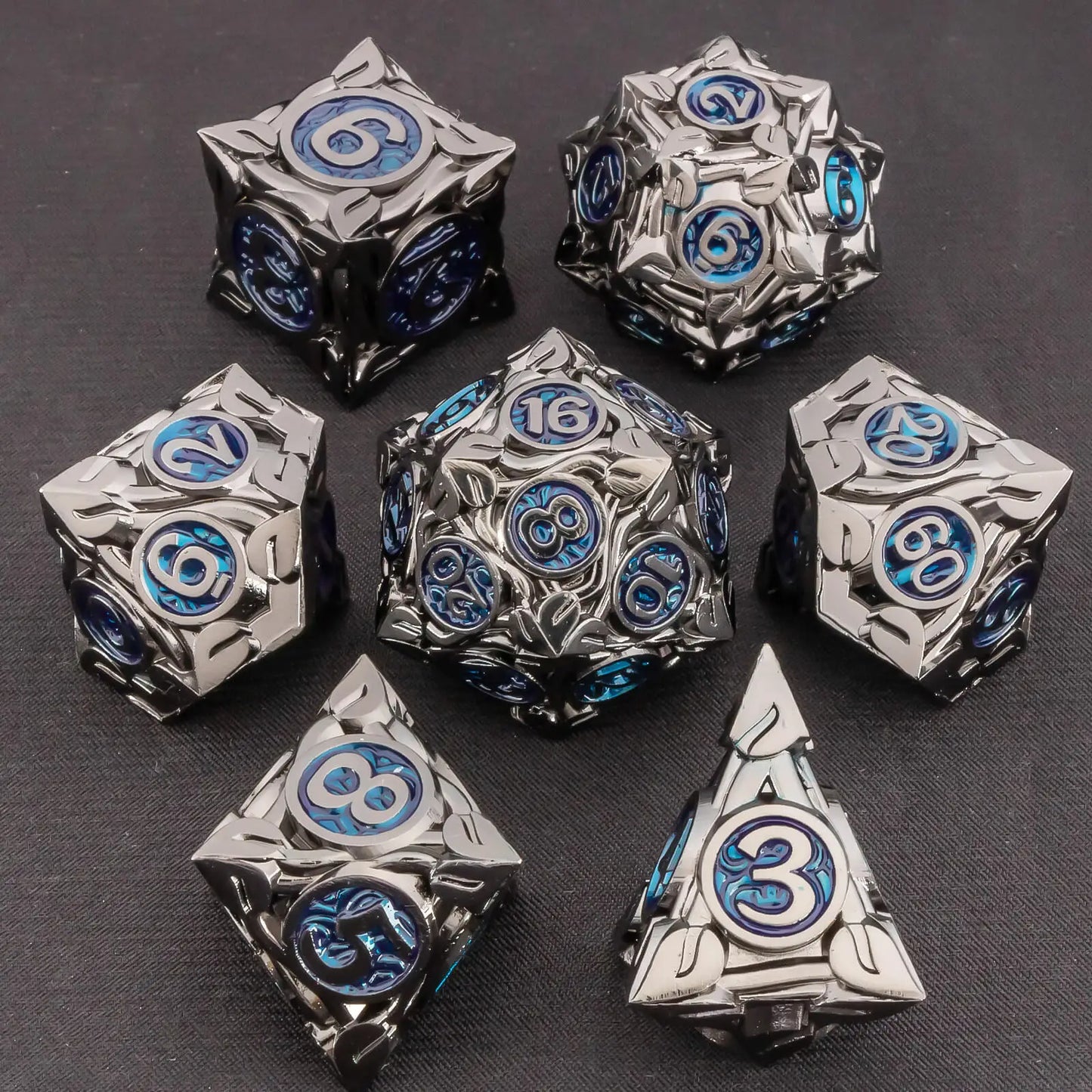 A set of metal fantasy tabletop gaming dice in a dark metallic silver finish with blue and black engraved details, arranged on a dark textured background.