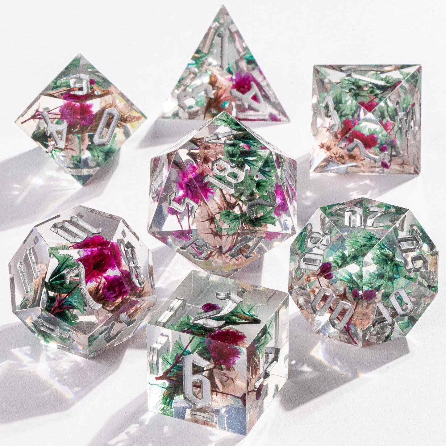 Set of transparent polyhedral dice with floral embedded design on a white background