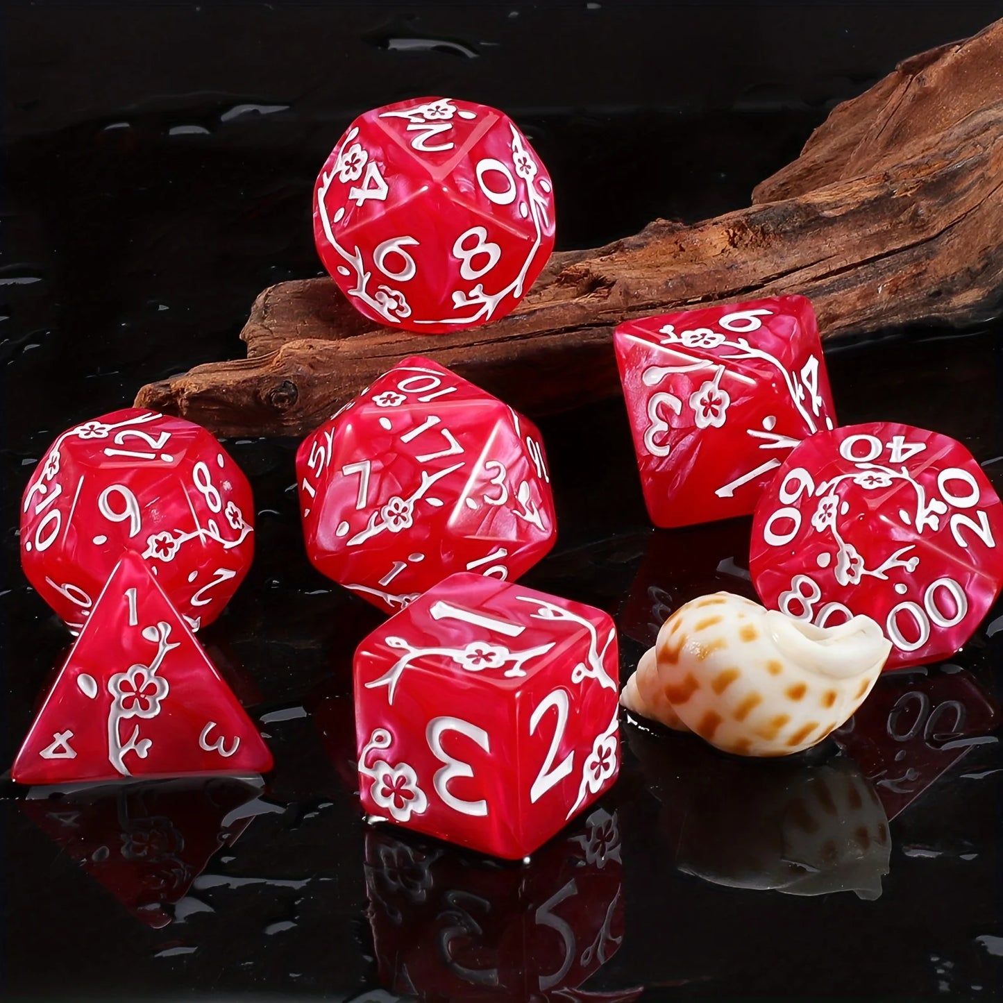 A set of red polyhedral dice with white floral engravings, arranged on a glossy black surface with a piece of driftwood and a small seashell prop.