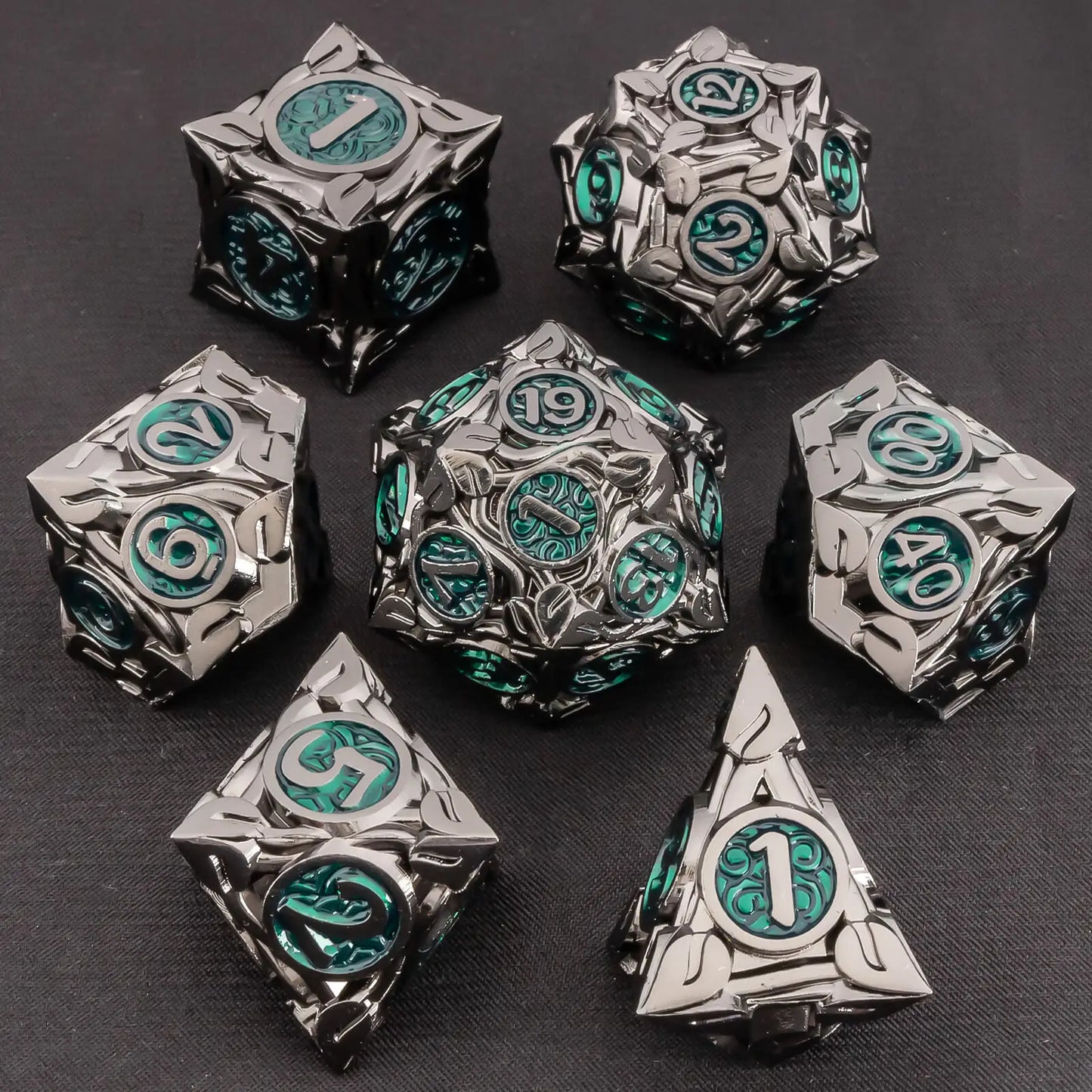 A set of ornate metal polyhedral gaming dice with a dark metallic finish and glowing green circular faces, arranged on a dark textured background.