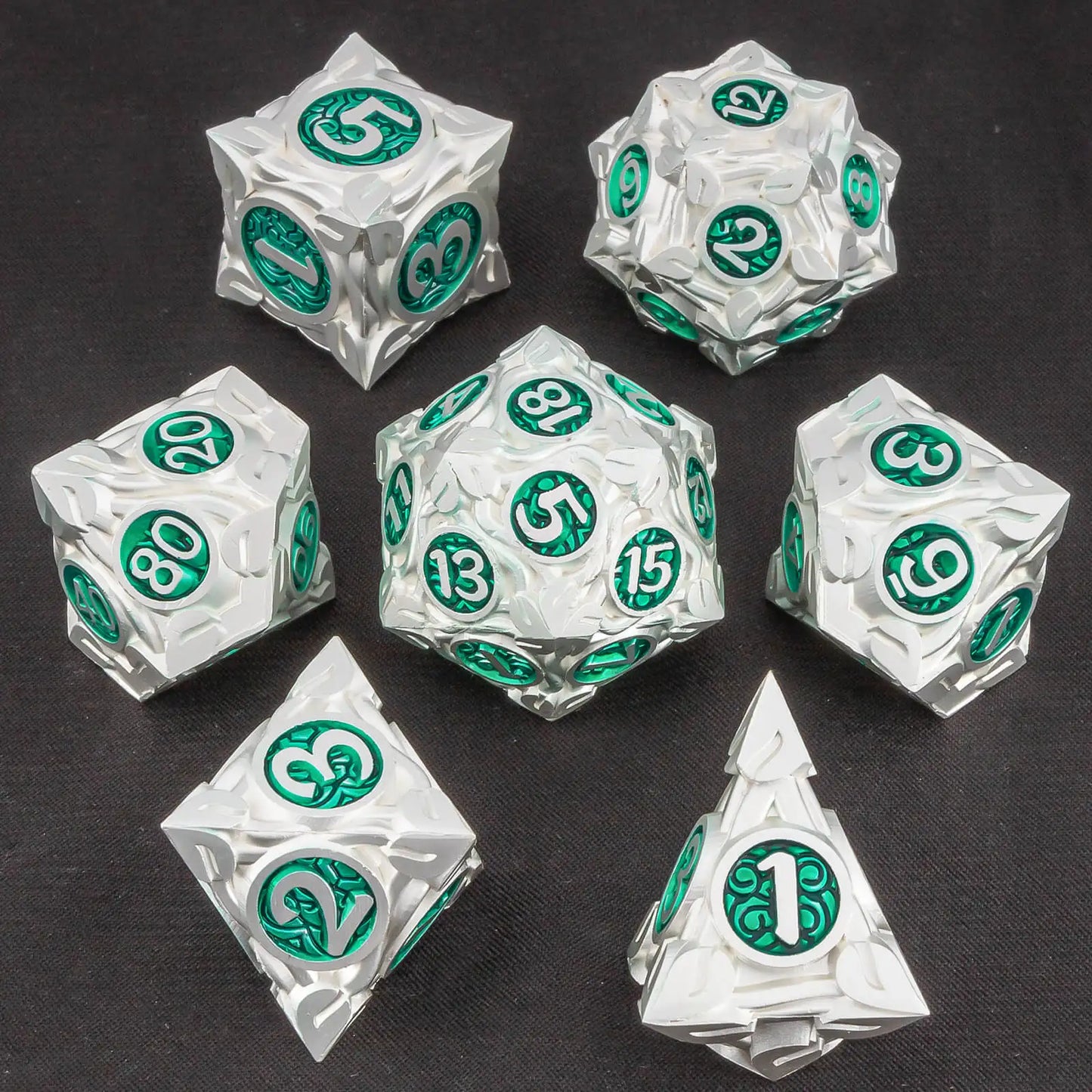 A set of seven metallic silver polyhedral gaming dice with green circular number pads, arranged on a dark textured background.