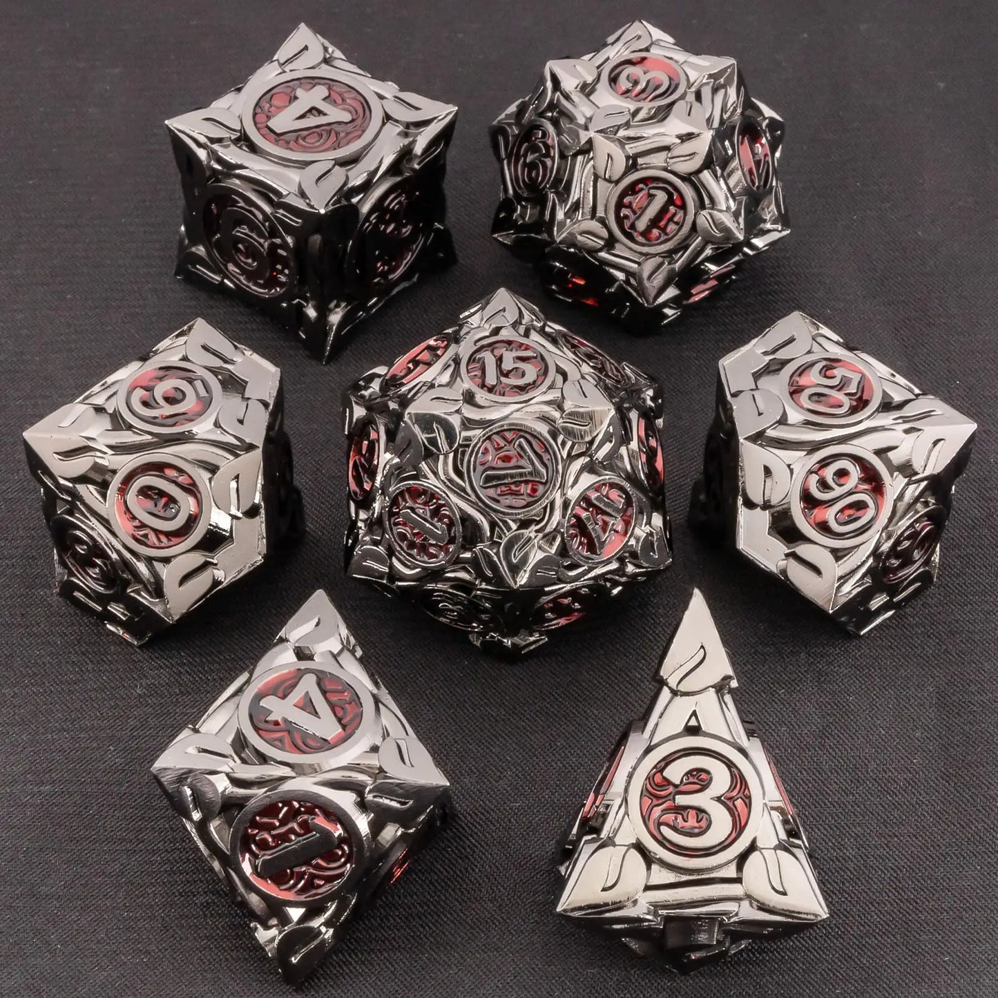A set of metallic fantasy dice with a polished dark metal finish and red engraved details, displayed on a dark textured background.