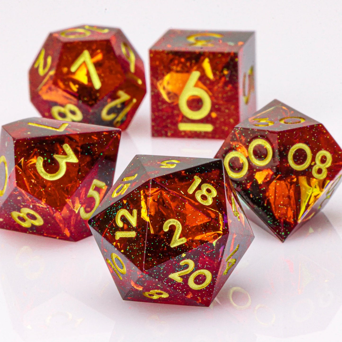 Set of polyhedral dice with red and orange glittery finish and yellow numbers on a white background