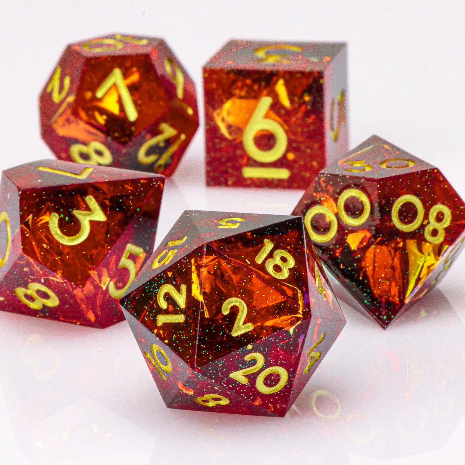 Set of polyhedral dice with red and orange glittery finish and yellow numbers on a white background