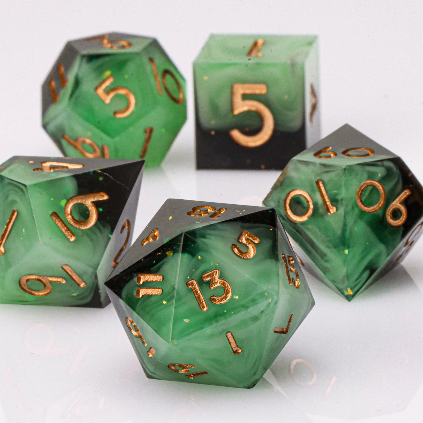 Set of green polyhedral dice with gold numbers on a white background