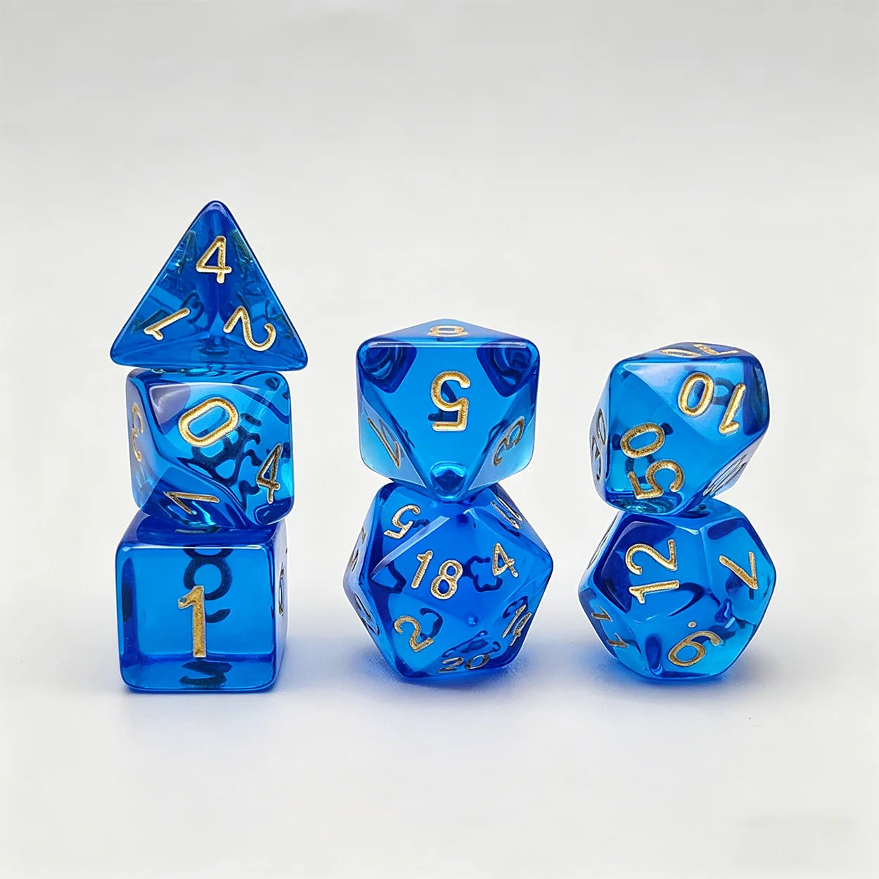 A set of translucent blue polyhedral gaming dice with shiny gold numbers, arranged in three stacks on a light gray background.