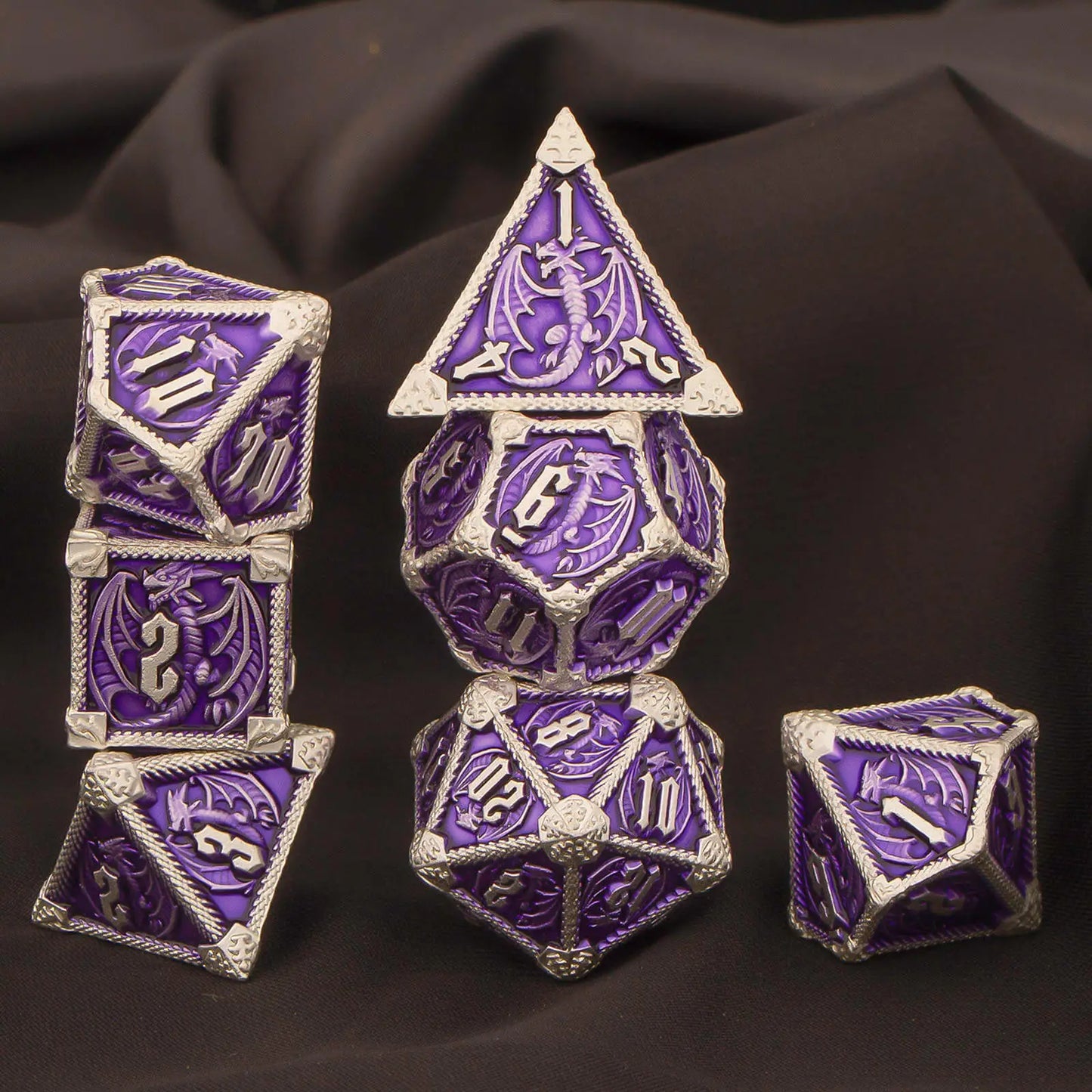 A set of metal purple and silver polyhedral gaming dice with dragon motifs, displayed on a dark draped fabric background.