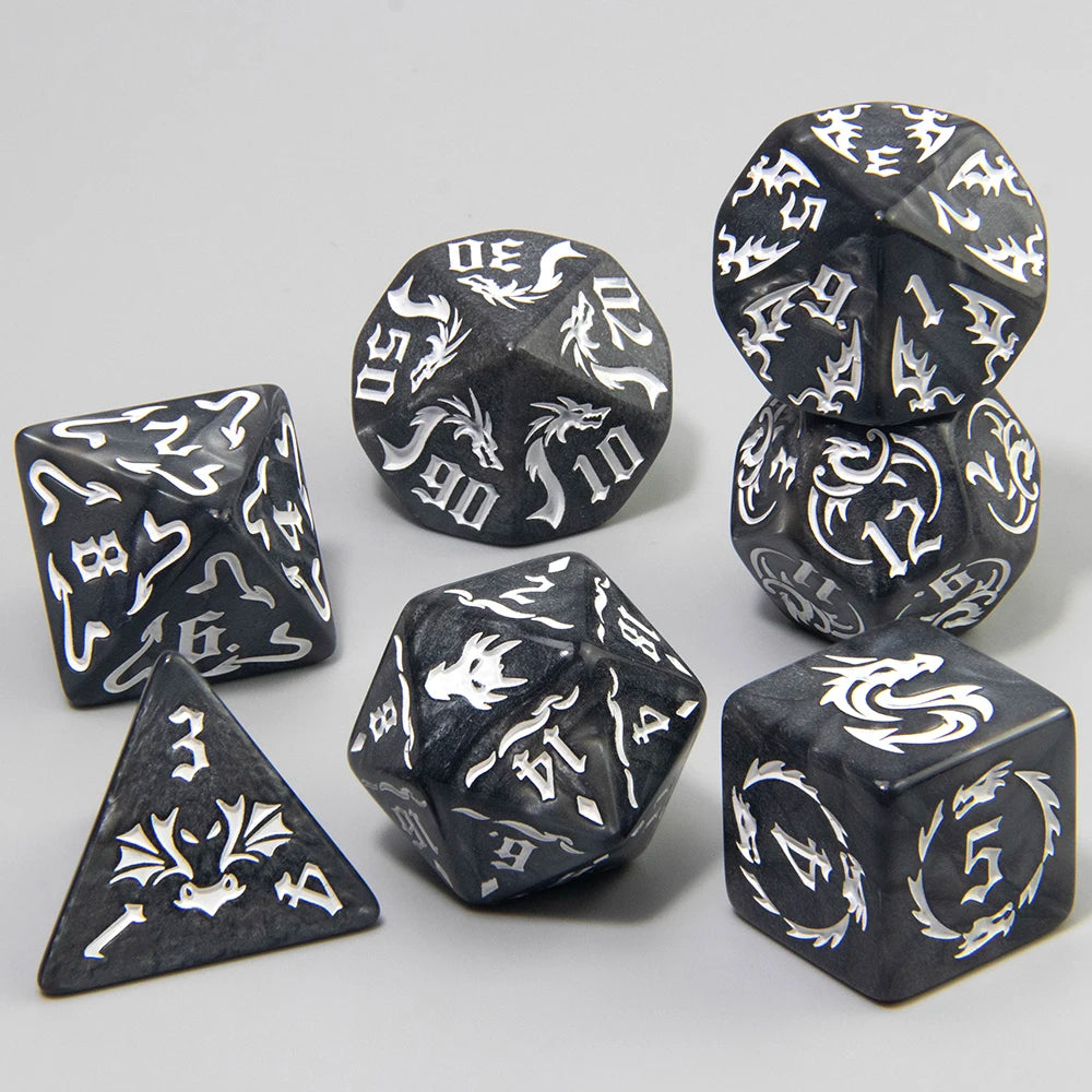 A set of black polyhedral gaming dice with white gothic-style dragon illustrations and white numbering, arranged on a light gray background.