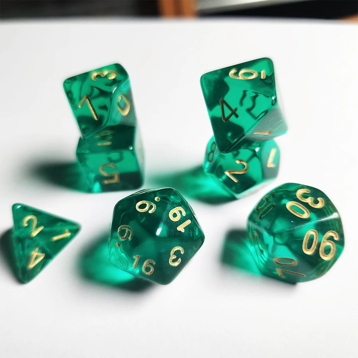 Set of green polyhedral dice with gold numbers on a white background