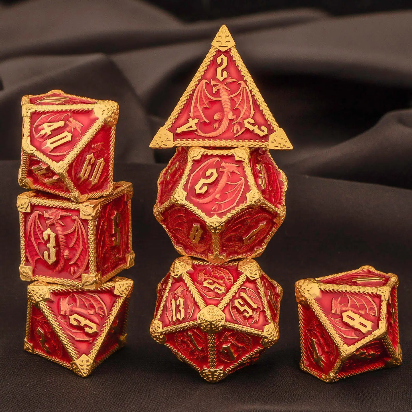 A set of metal red and gold fantasy-themed polyhedral dice displayed on a dark draped fabric background. The dice feature embossed red dragon motifs and raised gold borders, with gold numbers visible on the faces.