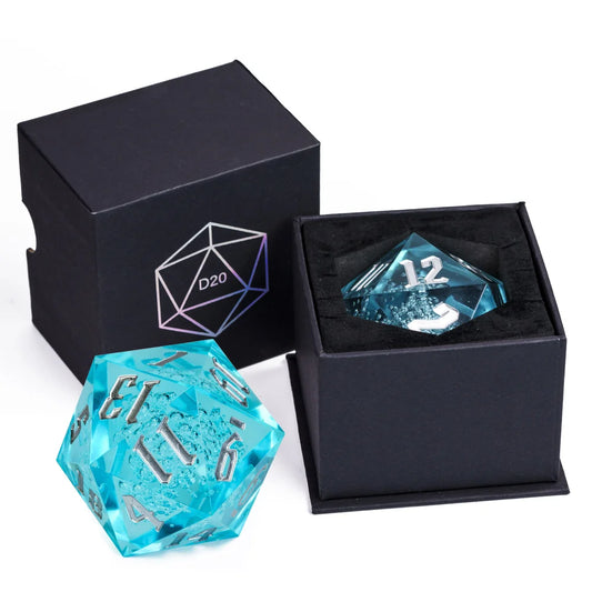 A translucent aqua blue 20-sided die (D20) shown next to its black presentation box, with a second view of the same die resting inside the open box on a black insert.