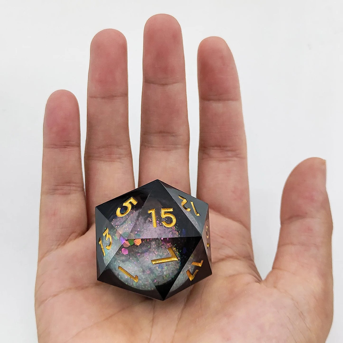 Black polyhedral dice with gold numbers held in a hand against a white background