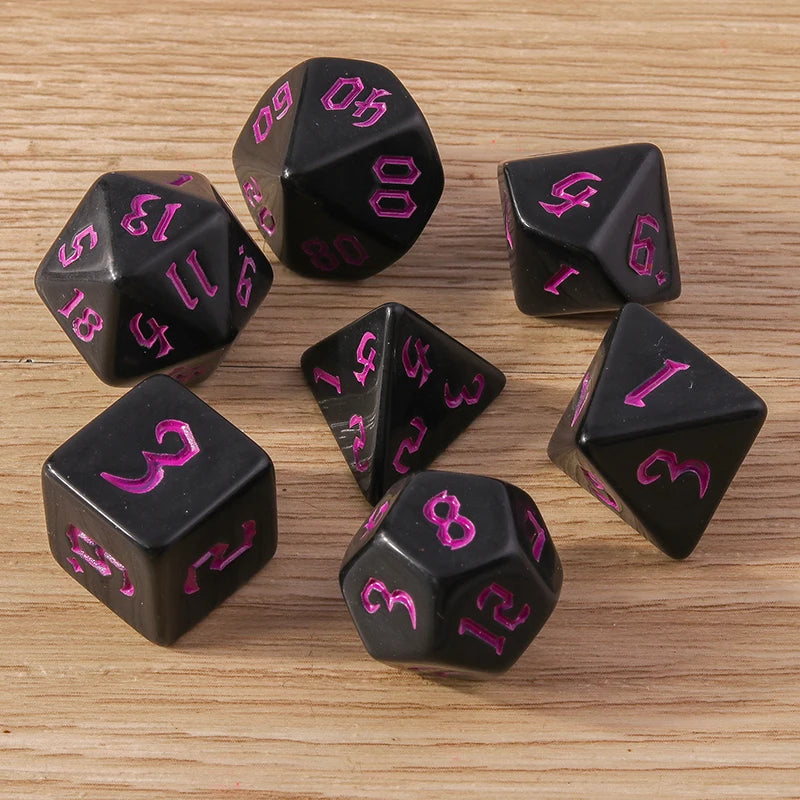 Black polyhedral dice set with pink numbers on a wooden surface